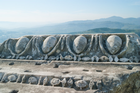 Part of old column with ionic ornament in the ancient Greek city of Pergamon with beautiful mountains on backgroundの写真素材