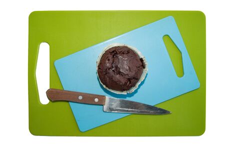 chocolate cupcake and knife on blue and green chopping board isolated on a white backgroundの写真素材