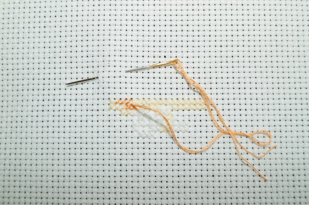 cross-stitch on a white canvas orange thread close-upの写真素材
