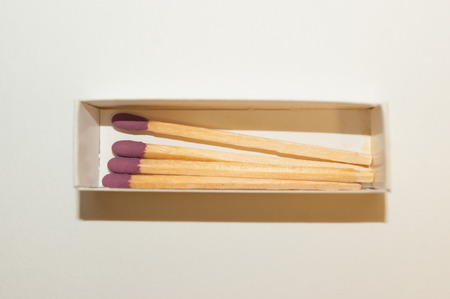 Four matches with purple heads in white matchbox close-up on white backgroundの写真素材