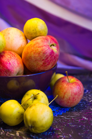 pink apples and small yellow apples in the bowl on a purple lacy napkinの写真素材