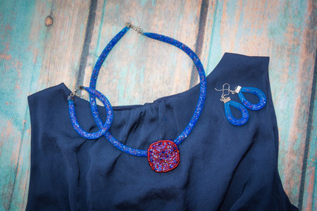 Necklace with red beaded pendant, bracelet and earrings of the blue harnesses, made of beads and jewelry grid lies on a blue satin dress on the backdrop of blue old wooden surfaceの写真素材
