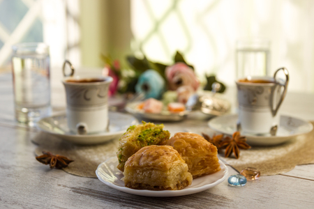 Two cups of Turkish coffee and glasses of water and a plate with baklava lukum in lukumluk decorative flowers and badyan on a sunny day on a wooden table vintage toned picture close-up shallow depth of fieldの写真素材