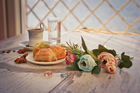 Cup of Turkish coffee and glasses of water and a plate with baklava lukum in lukumluk decorative flowers and badyan on a sunny day on a wooden table vintage toned picture close-up shallow depth of fieldの写真素材