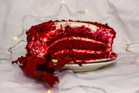 Homemade red velvet cake cut lies on a white tablecloth with garland and bokeh next to it is dry red leaf close-up shallow depth of fieldの写真素材