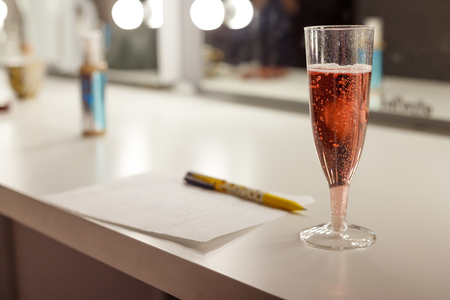 Glass of pink sparkling wine and note on a sheet in cage. Toned image with shallow depth of field, makeup artist's mirror on background.の写真素材