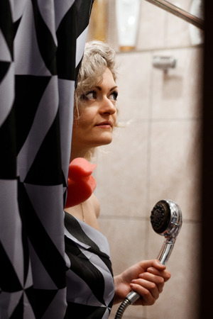 young woman in shower covered with a shower curtain wears a pink shower cap and holds a duck-shaped sponge. Toned image with grain and shallow depth of fieldの写真素材