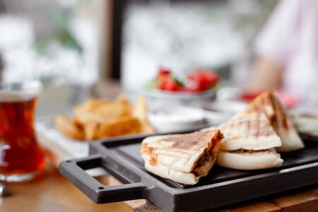 quesadilla sandwich with meat lies on black board on table in outdoor cafe. Turkish tea in glass, potatoes and vegetable salad next to it. Close-up toned image. Shallow depth of field, blurred backgroundの写真素材