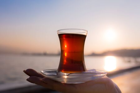 tea in traditional turkish glass on the female palm at dawn against the backdrop of the gulf of...
