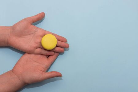 Macaroon cookie on female palm on blue flat background. Picture with copy space