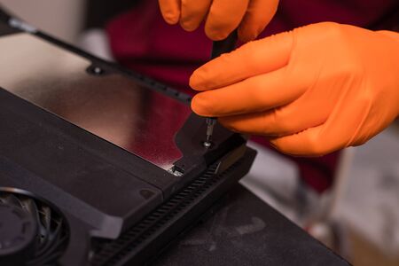 SAINT-PETERSBURG, RUSSIA, OCTOBER 27 2019: Man in orange gloves parses the PlayStation 4 Pro console...