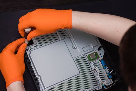 SAINT-PETERSBURG, RUSSIA, OCTOBER 27 2019: Man in orange gloves parses the PlayStation 4 Pro console...