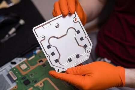 SAINT-PETERSBURG, RUSSIA, OCTOBER 27 2019: Man in orange gloves parses the PlayStation 4 Pro console. Close-up, shallow depth of fieldのeditorial素材