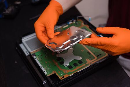 SAINT-PETERSBURG, RUSSIA, OCTOBER 27 2019: Man in orange gloves parses the PlayStation 4 Pro...