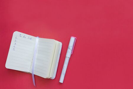 Notepad with to-do list written on page and pen with trendy marble pattern on pink background top...