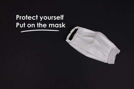 Origami paper medical protective mask flat lay with copy space. Chalk inscription Protect yourself, Put on the mask. Coronavirus COVID-19 cause deficit of medical masks in pharmacies.の写真素材