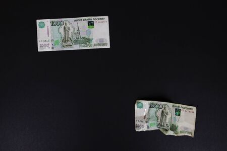 Smooth and wrinkled banknotes thousand Russian Rubles top view on black background. Ruble collapse....