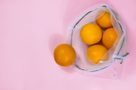 Oranges in mesh bag flat lay on pink background. Picture with selective focus and copy space....