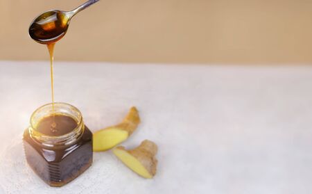 Buckwheat honey pours from spoon into jar and sliced ginger lying near. Natural medicine, healthy...