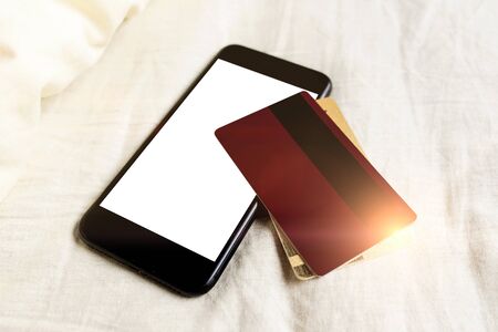 Online shopping concept. Pay for subscriptions. Smartphone with credit cards rumpled bed. Stay home due quarantine. Online call. Telemedicine. White mock-up blank screen.の写真素材