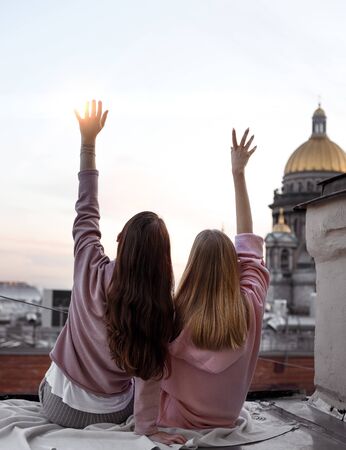 Two girls are sitting back view on the roof in the center of St. Petersburg, Russia. View of St. Isaac's Cathedral. Traveling with friends. Walks on the roof. White Nightsの写真素材