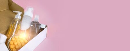 Delivery of skin care cosmetics. Facial wash gel, soap and other cosmetics in box. Flat lay on pink...