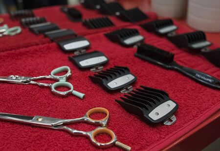 Hairdresser tools flat lay on red towel. Preparing for haircut. Nozzles for hair clippers and scissors. Close-up shallow depth of field.の写真素材