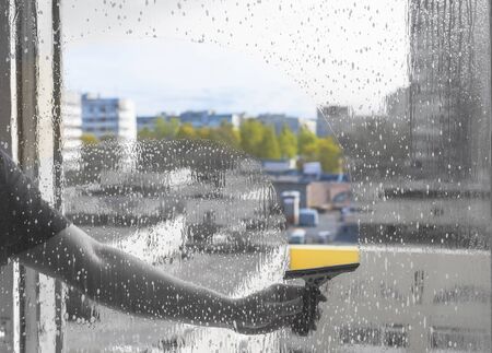 Rubber squeegee in male hand cleans soaped window. Picture with selective focus. Washing windows....