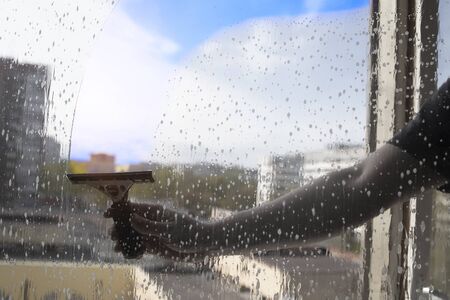 Rubber squeegee in male hand cleans soaped window. Picture with selective focus. Washing windows. Leaves a clear, saturated transparent streak against the background of dim monochrome surroundingsの写真素材