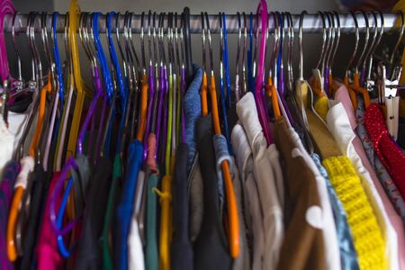 Women's wardrobe close-up shallow depth of field. Closet is tightly packed with clothes on multi-colored hangers. Disorganized wardrobeの写真素材