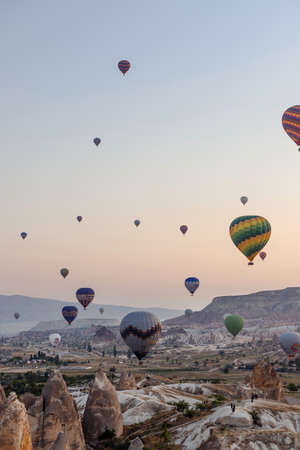 Goreme, Cappadocia, Turkey â 23 August 2019: Many hot air balloons fly in sky at dawn. People look at them from the ground. Cappadocia Earth Pyramids. Tourism concept.のeditorial素材