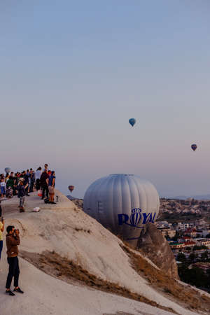 Goreme, Cappadocia, Turkey â 23 August 2019: Many hot air balloons blast off in sky at dawn. People look at them from the ground. Cappadocia Earth Pyramids. Tourism concept.のeditorial素材