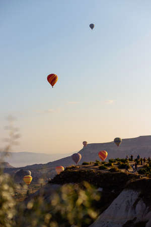Goreme, Cappadocia, Turkey â 22 August 2019: Many hot air balloons fly in sky at dawn. People look at them from the ground. Cappadocia Earth Pyramids. Tourism concept.のeditorial素材