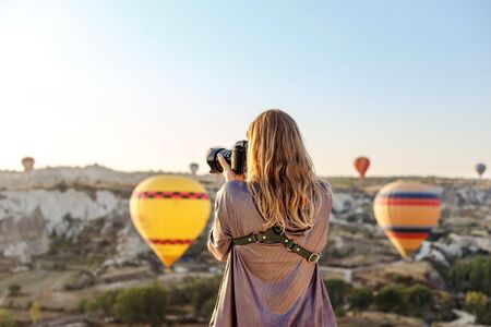 Woman photographer takes pictures of flying hot air balloon at dawn in Cappadocia, Turkey. Travel concept.の写真素材