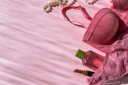 Lingerie bra and panties, body lotion bottle, lipstick and pearl beads. Pink flatlay top view with place for text. Picture with sunbeams. Taking care of yourself. Self-love. Fashionable modern girl stuffの写真素材