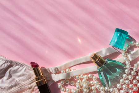 Lingerie garter for stockings, perfume bottle, lipstick and pearl beads. Pink flatlay top view with place for text. Picture with sunbeams. Taking care of yourself. Self-love. Fashionable modern girl stuffの写真素材