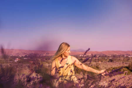 Blonde woman in a yellow dress in lavender field at sunset. Lavender bloom season. Enjoyment of unity with nature. Meditation and relaxation outdoorの写真素材