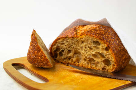 Freshly baked cereal bread on a wooden board under a white towel. Homemade baking. Healthy eating....