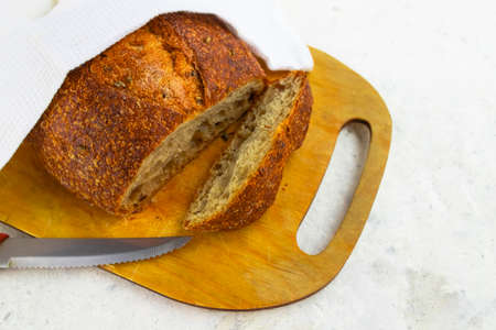 Freshly baked cereal bread on a wooden board under a white towel. Homemade baking. Healthy eating....