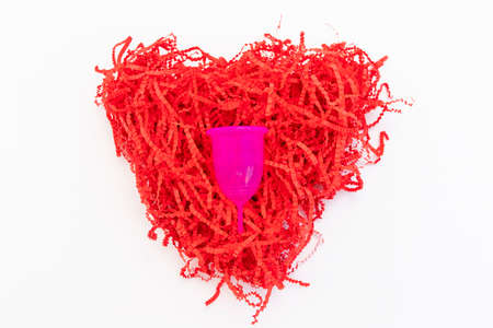 Menstrual cup in red shredded paper packaging material flat lay on white background. Zero waste...