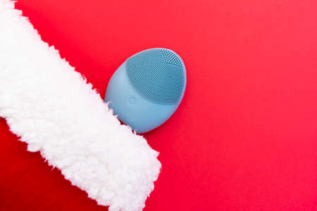Silicone brush for washing face and a Christmas hat. Facial cleansing brush as gift. Skincare concept. Brush for face lifting, anti-aging wrinkles and massage. Copy spaceの写真素材