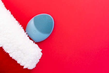 Silicone brush for washing face and a Christmas hat. Facial cleansing brush as gift. Skincare concept. Brush for face lifting, anti-aging wrinkles and massage. Copy spaceの写真素材