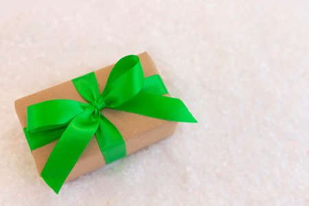 Gift wrapped in craft paper and decorated with green ribbon flat lay with snow on background. Top view picture with place for text and shallow depth of fieldの写真素材