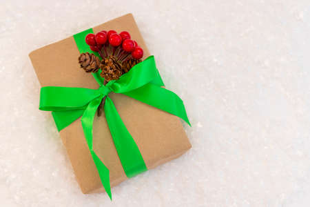Gift wrapped in craft paper and decorated with green ribbon flat lay with snow on background. Top view picture with place for text and shallow depth of fieldの写真素材