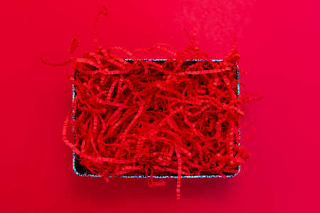 Red shredded paper packaging material in box flat lay on red background. Template for placing goods...
