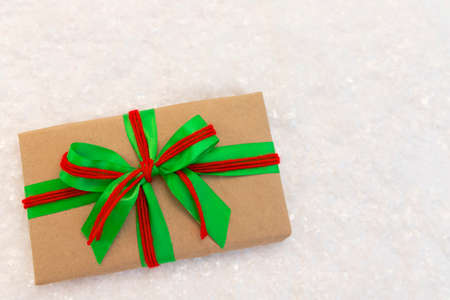 Gift wrapped in craft paper and decorated with green and red ribbon flat lay with snow on background. Top view picture with place for text and shallow depth of fieldの写真素材