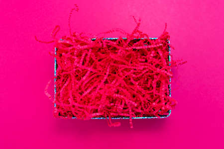Pink shredded paper packaging material in box flat lay on pink background. Template for placing goods or textの写真素材