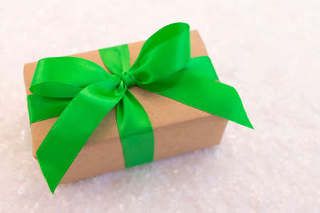 Gift wrapped in craft paper and decorated with green ribbon flat lay with snow on background. Top view picture with place for text and shallow depth of fieldの写真素材