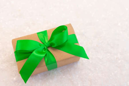 Gift wrapped in craft paper and decorated with green ribbon flat lay with snow on background. Top view picture with place for text and shallow depth of fieldの写真素材