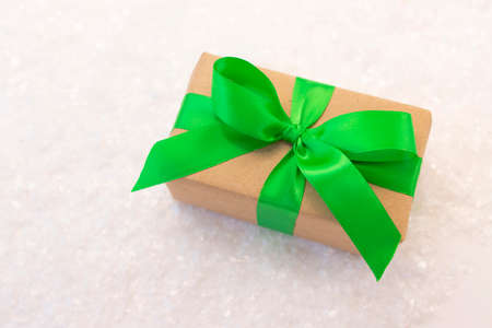 Gift wrapped in craft paper and decorated with green ribbon flat lay with snow on background. Top view picture with place for text and shallow depth of fieldの写真素材